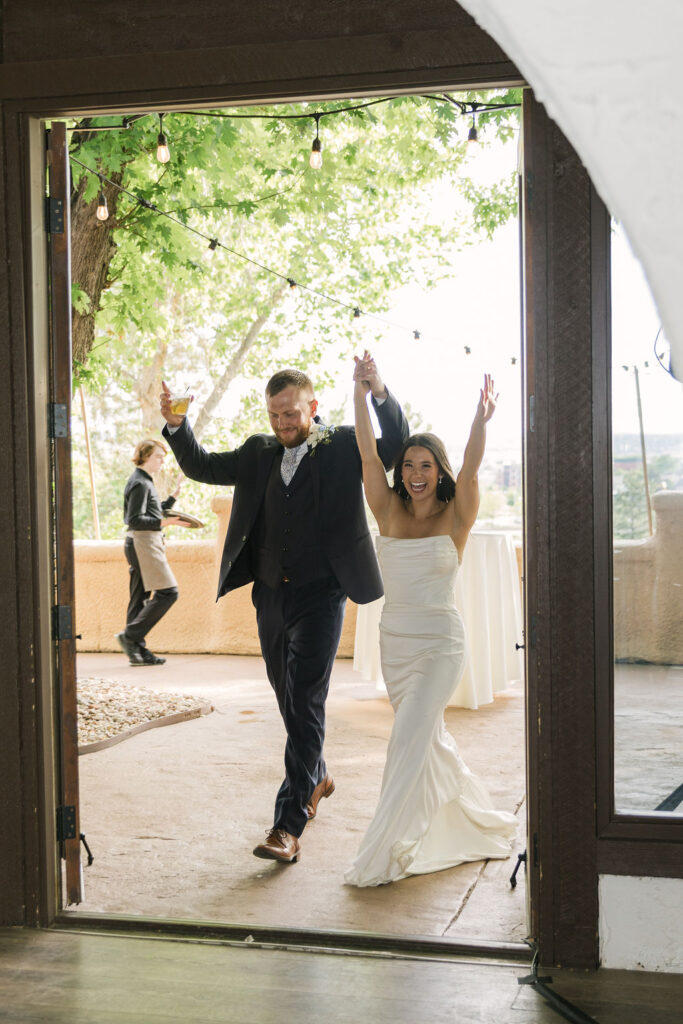 Bride and groom entering Villa Parker reception with hands raised.