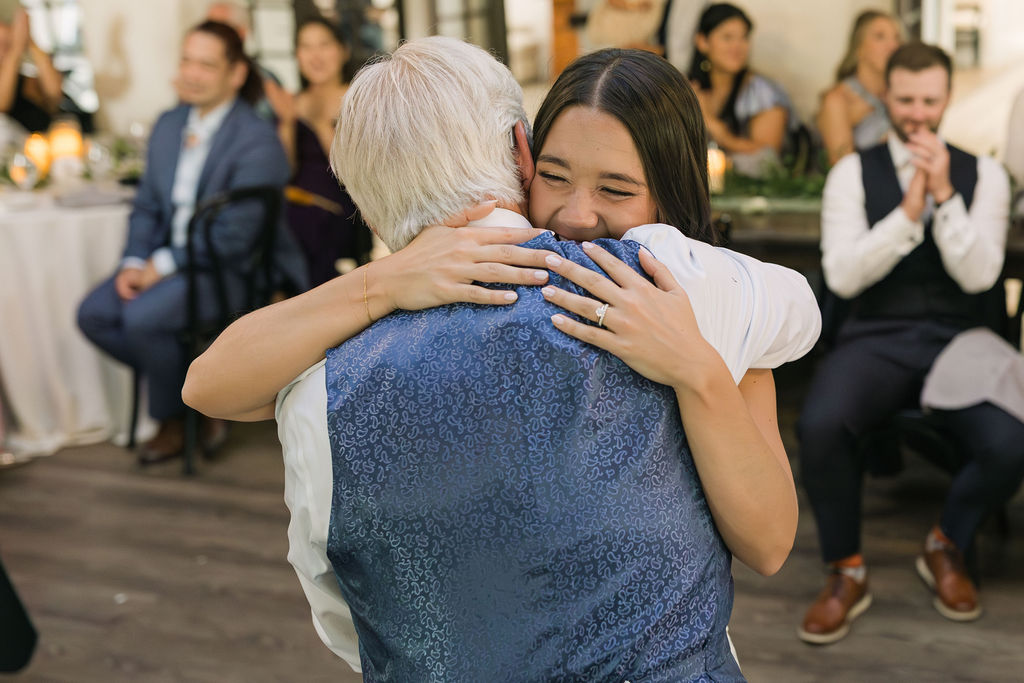Bride hugging dad during emotional reception moment.