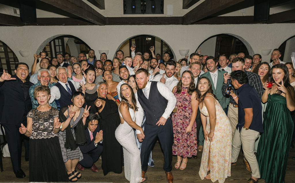 Large group photo of wedding guests gathered around the bride and groom inside Villa Parker’s European-inspired reception space during their Colorado wedding.