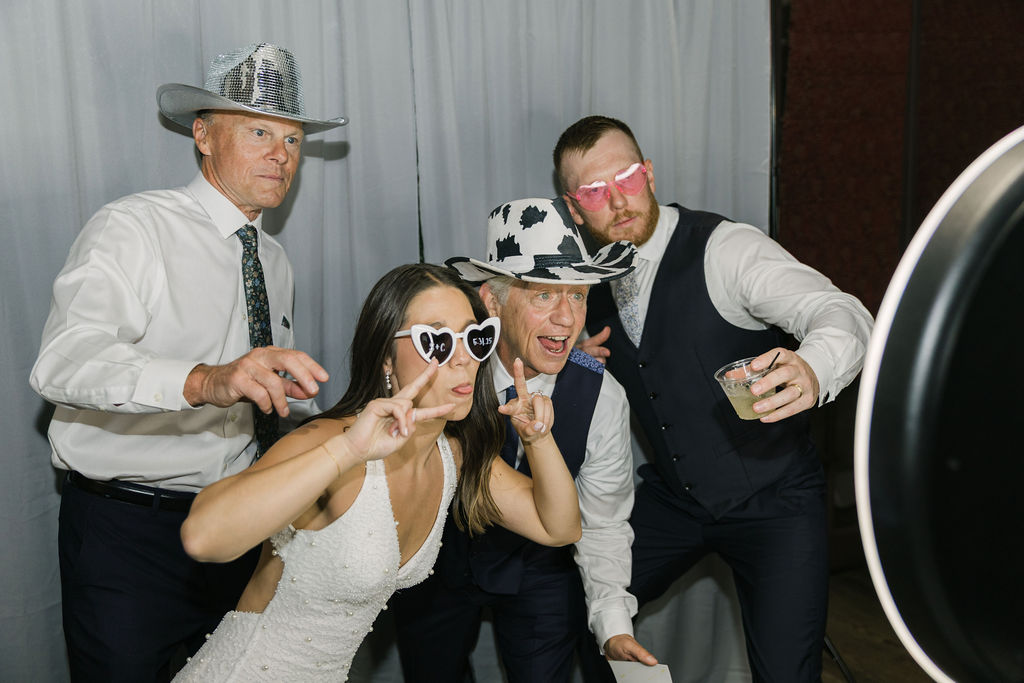 Bride and groom posing with guests using fun props at photo booth.