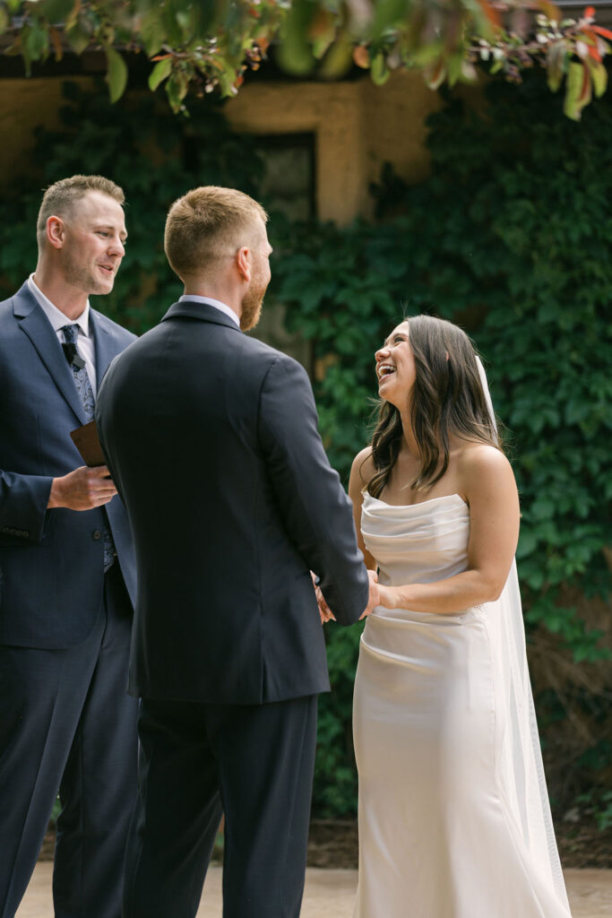 Bride laughing while holding hands with the groom during their outdoor ceremony at Villa Parker in Colorado.
