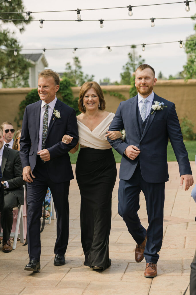 Groom walking down the aisle with his parents during the outdoor ceremony at Villa Parker, a European-inspired Colorado wedding venue.
