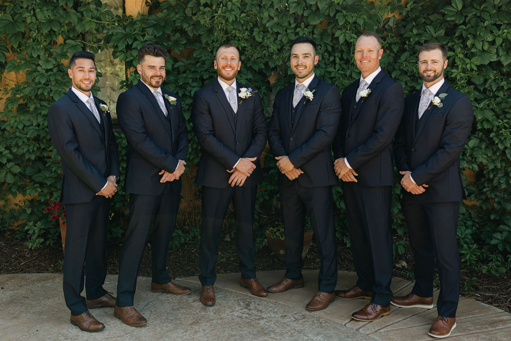 Groom standing with his groomsmen in front of lush greenery at Villa Parker, captured in classic Colorado wedding party portraits.