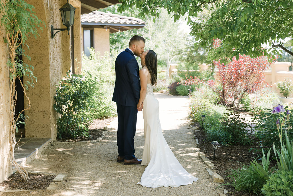 Bride and groom kissing on a flower lined walkway during Colorado garden wedding portraits.
