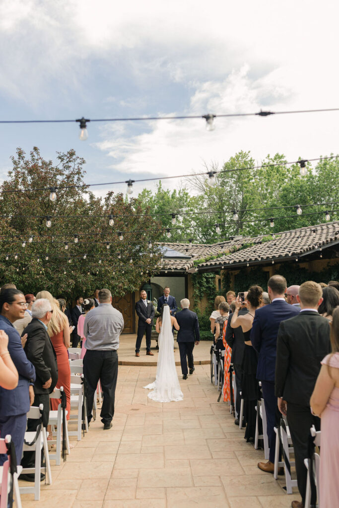 Wide view of the outdoor ceremony setup at Villa Parker with guests seated under bistro lights during this Colorado wedding.