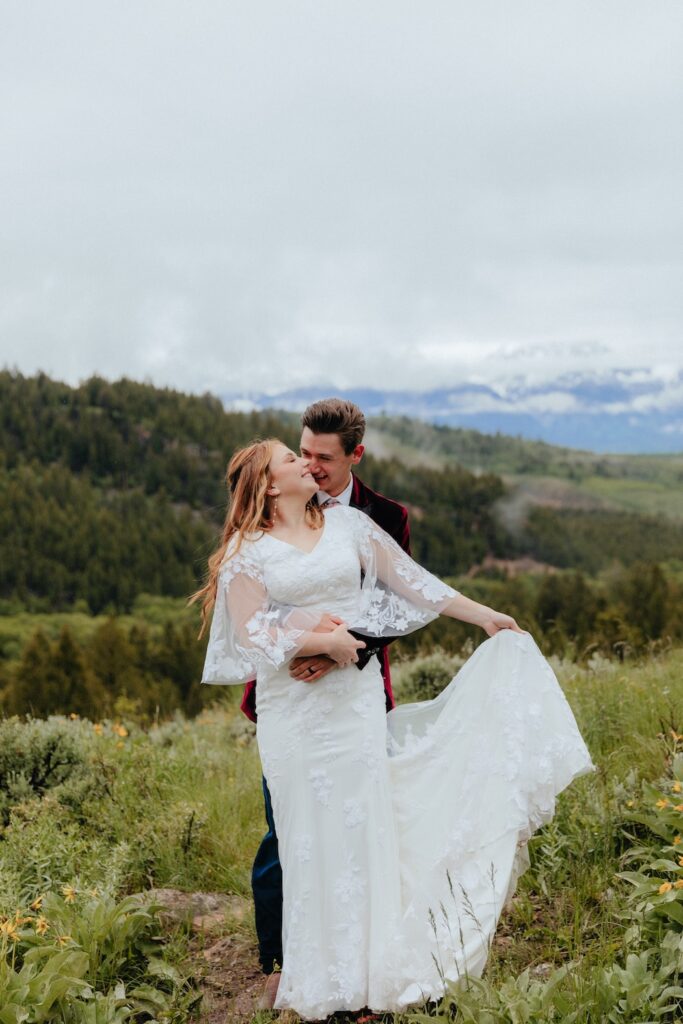Candid photo of bride and groom hugging with the Grand Tetons behind them 