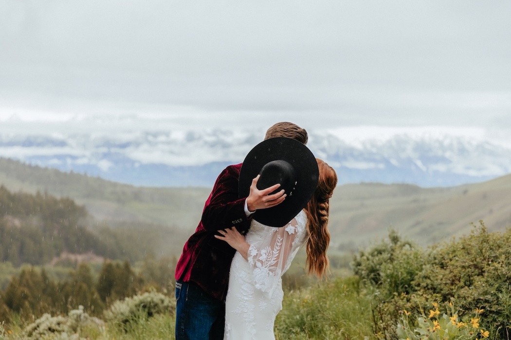 Bride and groom sharing their first kiss underneath his cowboy hat at the Wedding Tree with the Grand Tetons in the background