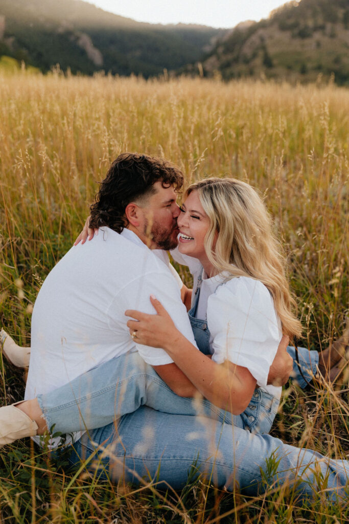 casual golden hour field engagement photos of the couple in white t-shirts and denim at Chautauqua Park