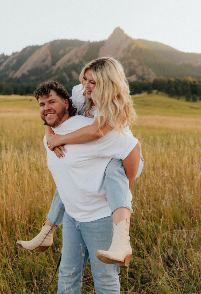 casual golden hour field engagement photos of the couple in white t-shirts and denim at Chautauqua Park