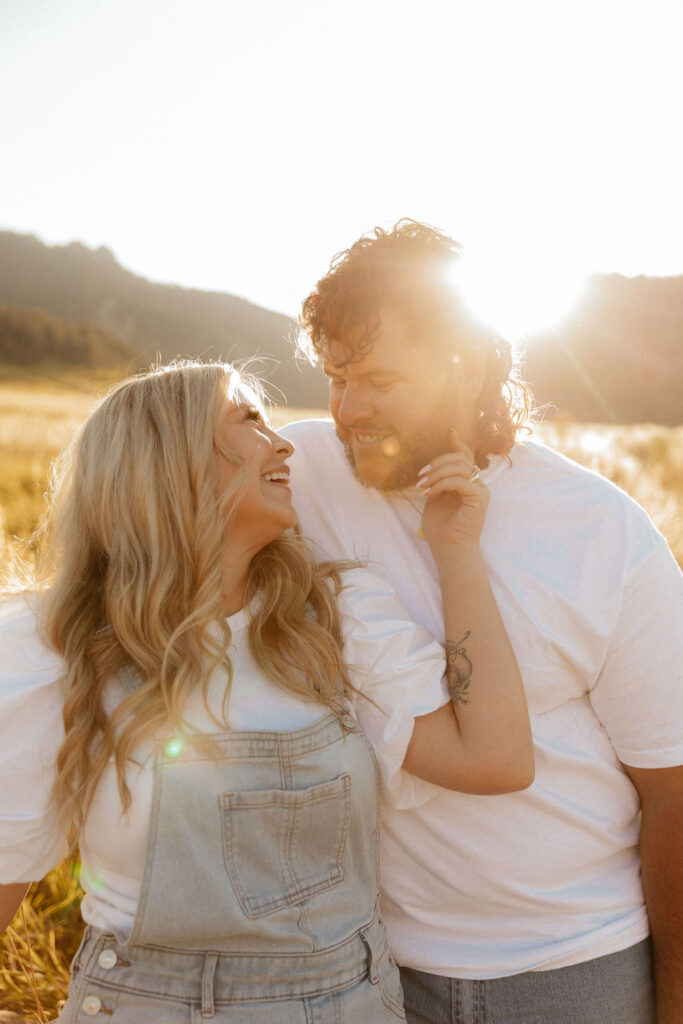 casual golden hour field engagement photos of the couple in white t-shirts and denim at Chautauqua Park