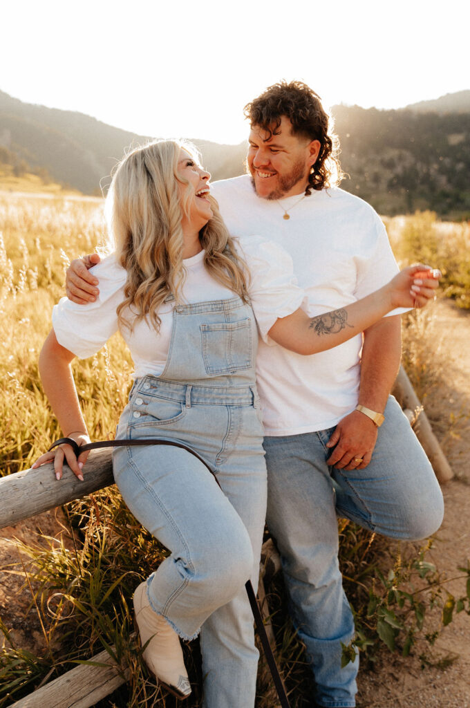 casual golden hour field engagement photos of the couple in white t-shirts and denim at Chautauqua Park