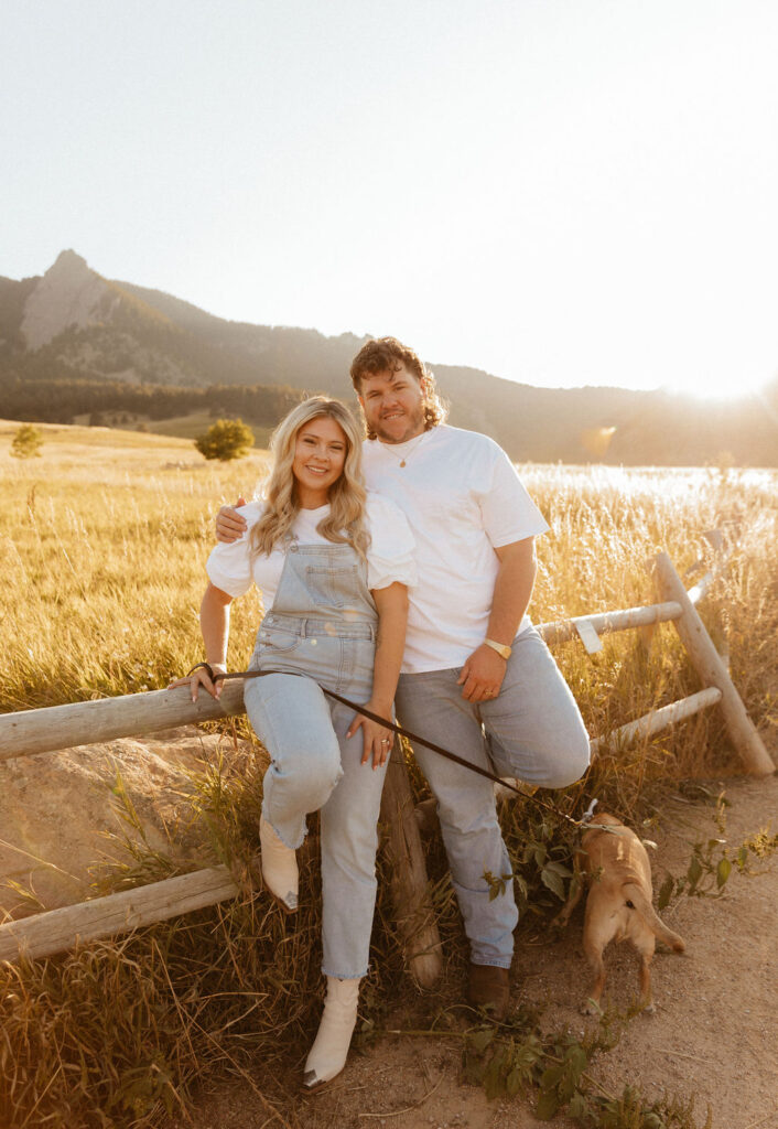 casual golden hour field engagement photos of the couple in white t-shirts and denim with their pug at Chautauqua Park