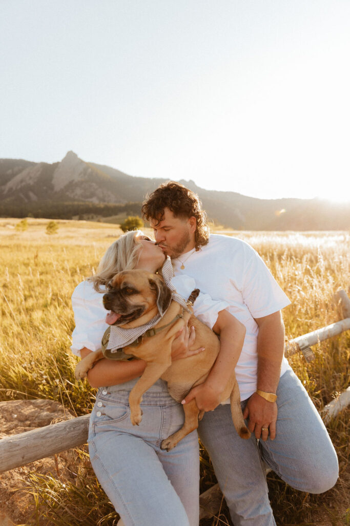 casual golden hour field engagement photos of the couple in white t-shirts and denim with their pug at Chautauqua Park