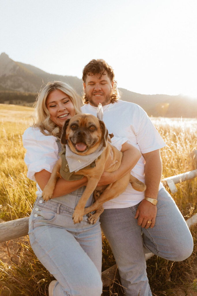 casual golden hour field engagement photos of the couple in white t-shirts and denim with their pug at Chautauqua Park