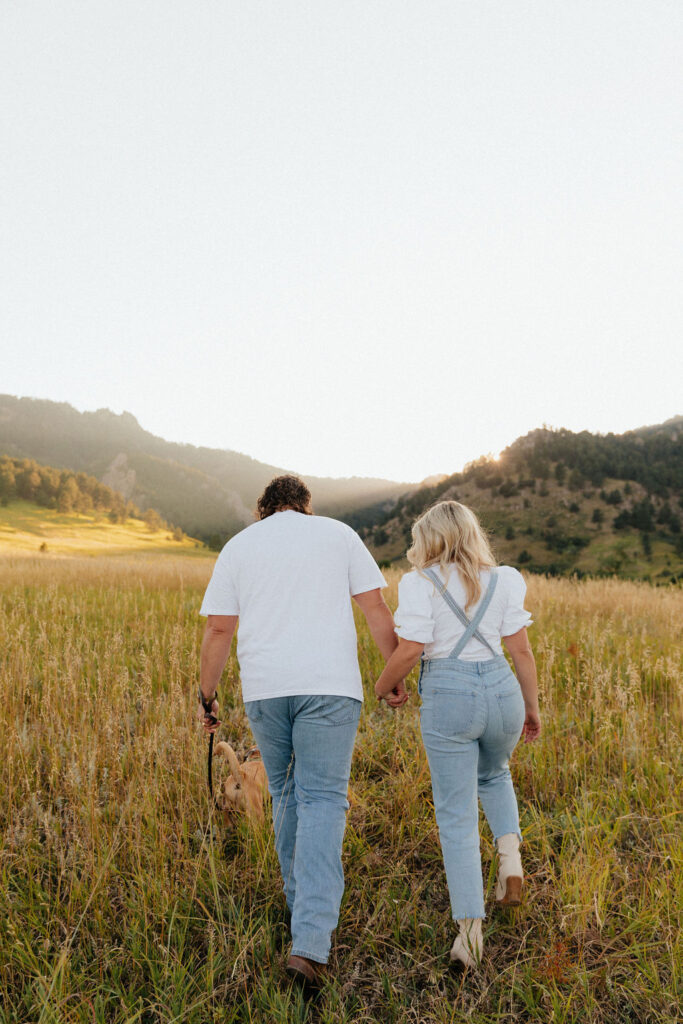 casual golden hour field engagement photos of the couple in white t-shirts and denim with their pug at Chautauqua Park