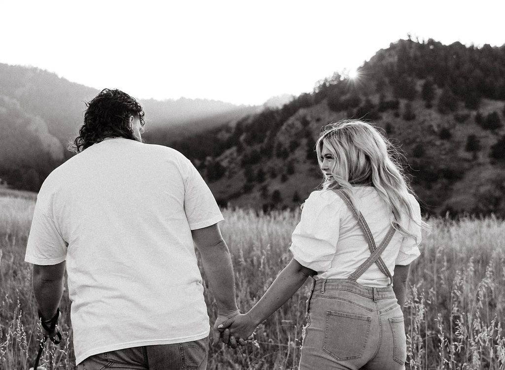 casual golden hour field engagement photos of the couple in white t-shirts and denim at Chautauqua Park