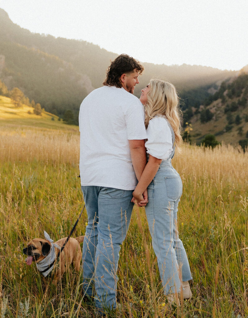 casual golden hour field engagement photos of the couple in white t-shirts and denim with their pug at Chautauqua Park