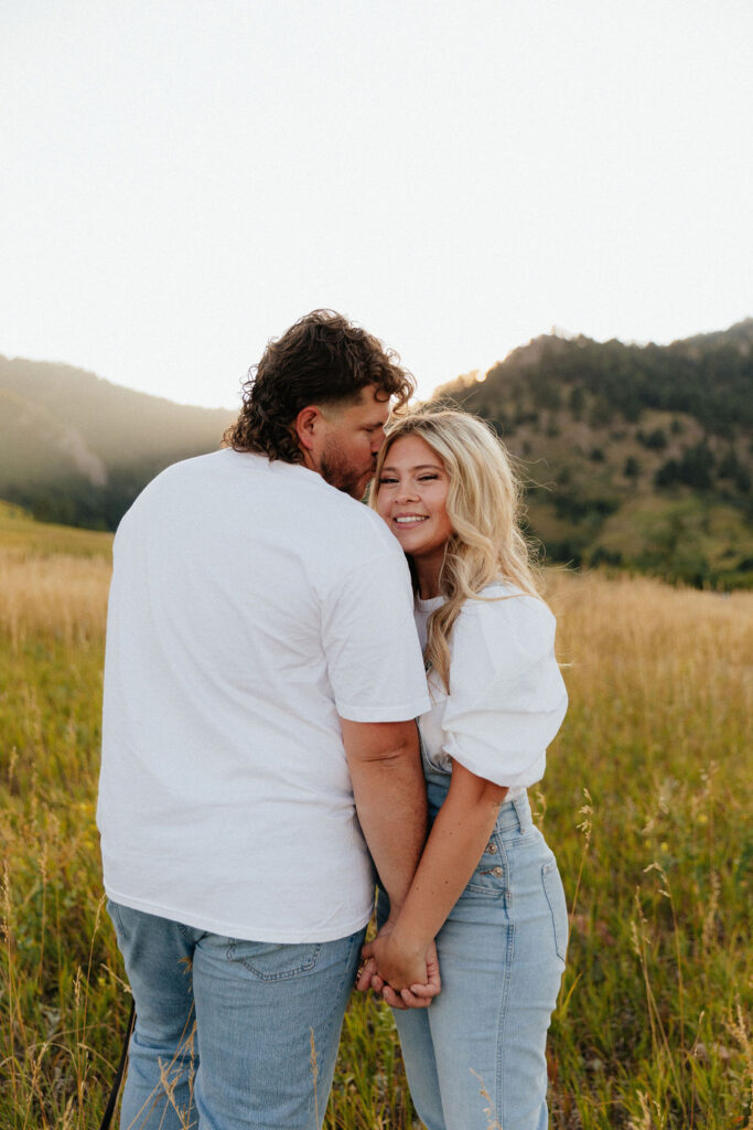 casual golden hour field engagement photos of the couple in white t-shirts and denim at Chautauqua Park