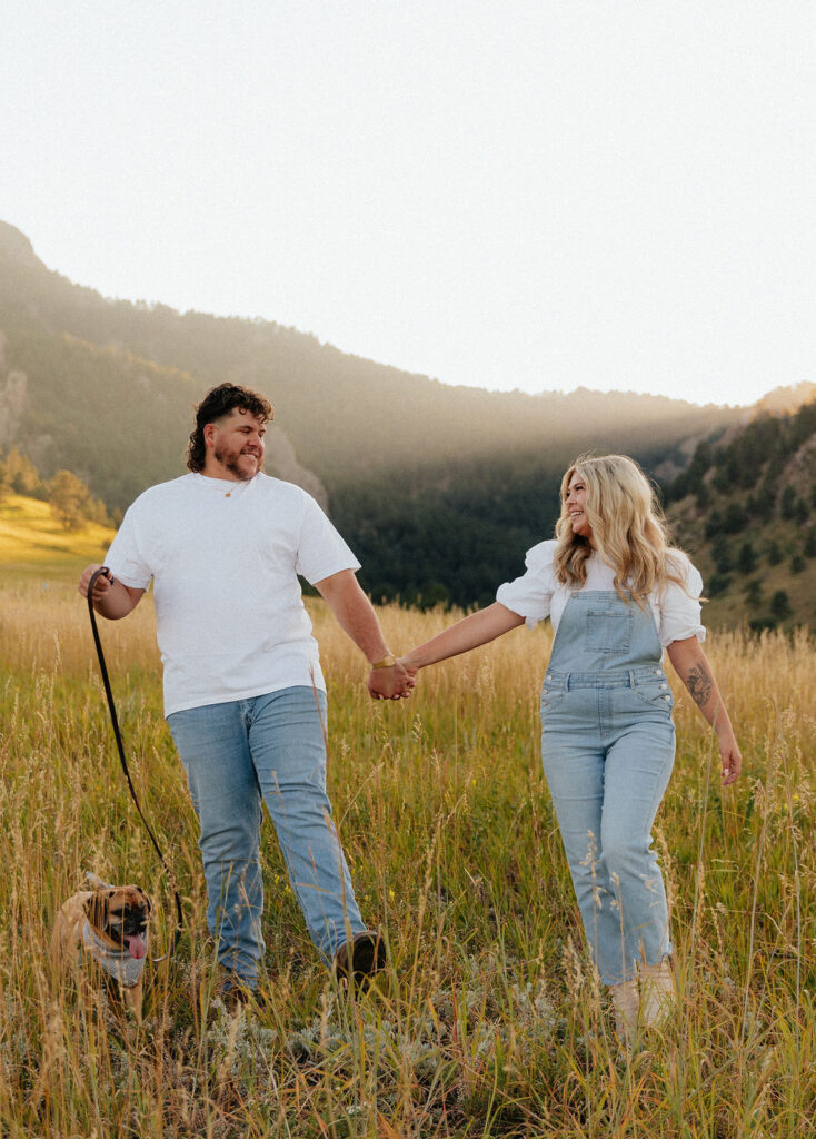 casual golden hour field engagement photos of the couple in white t-shirts and denim with their pug at Chautauqua Park