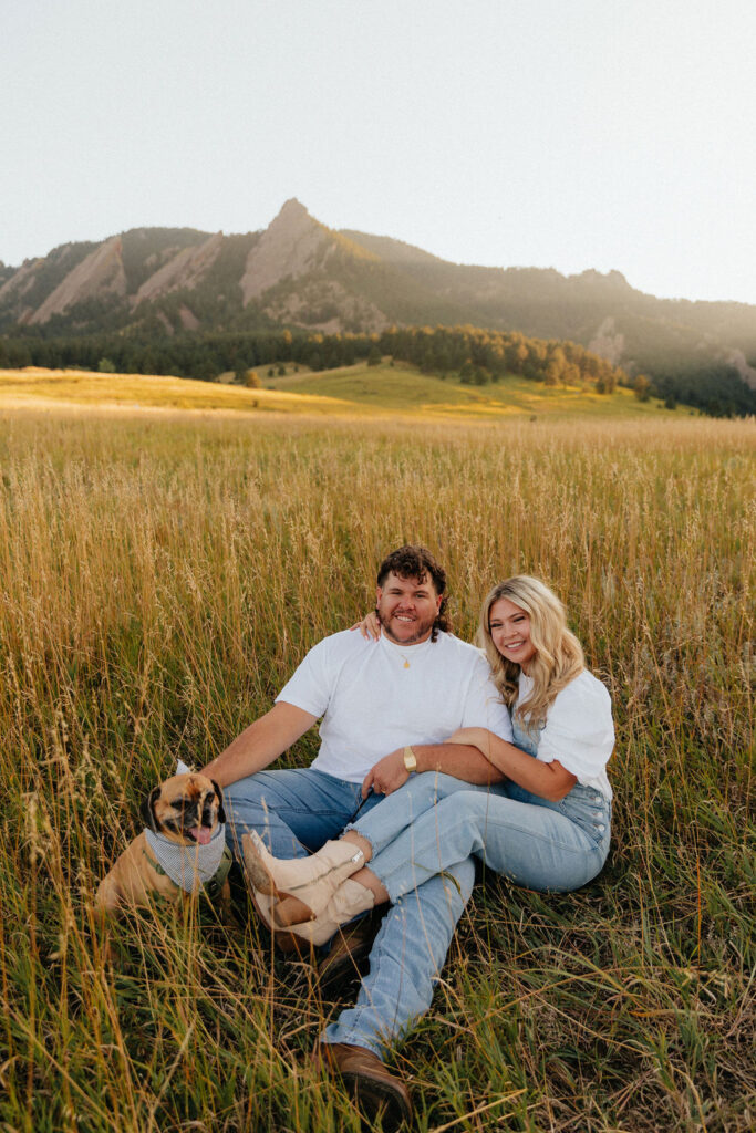 casual golden hour field engagement photos of the couple in white t-shirts and denim with their pug at Chautauqua Park