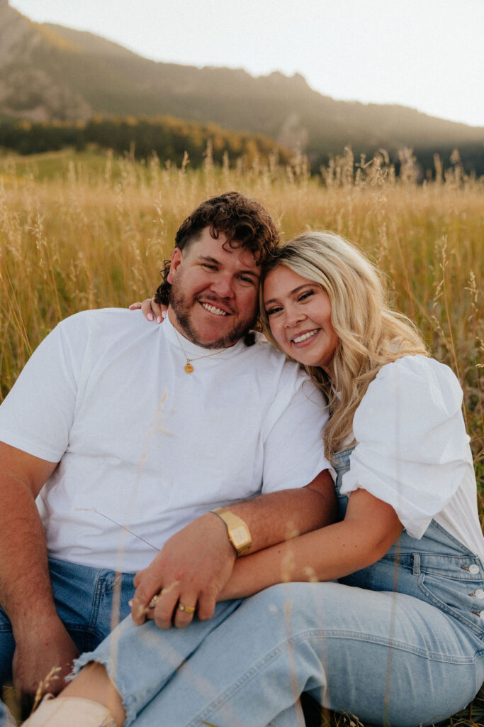 casual golden hour field engagement photos of the couple in white t-shirts and denim at Chautauqua Park