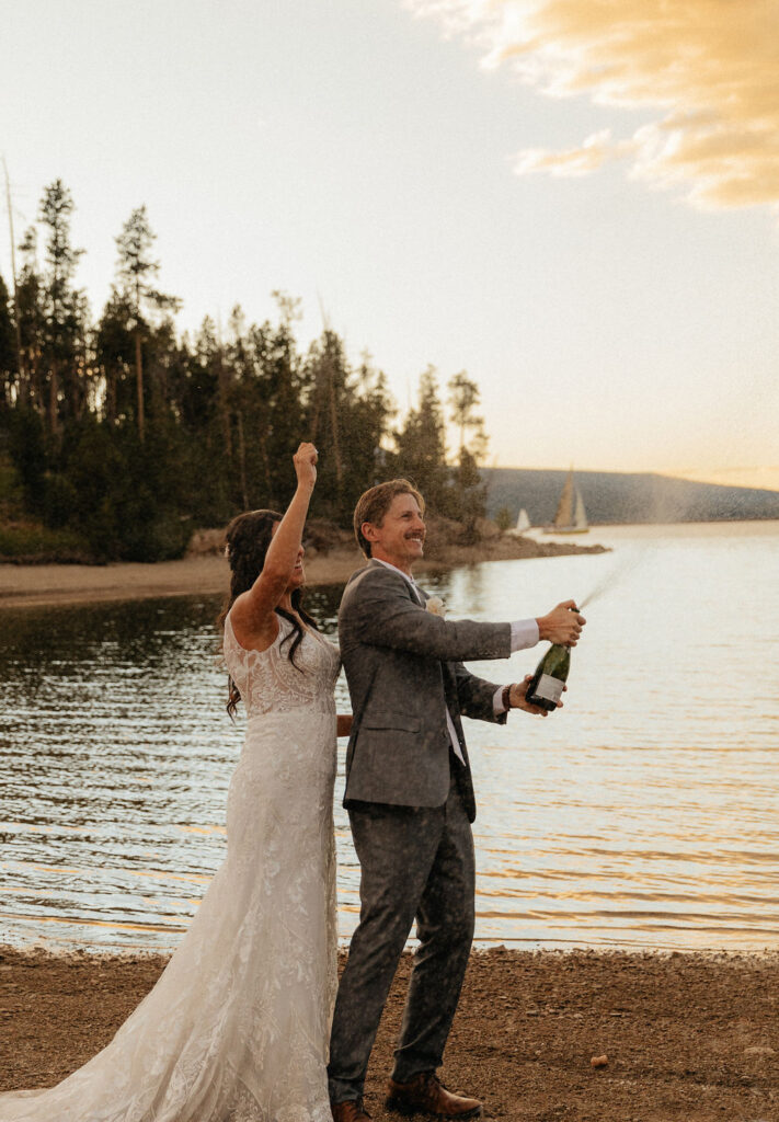 bride and groom popping a bottle of champagne at lake dillon