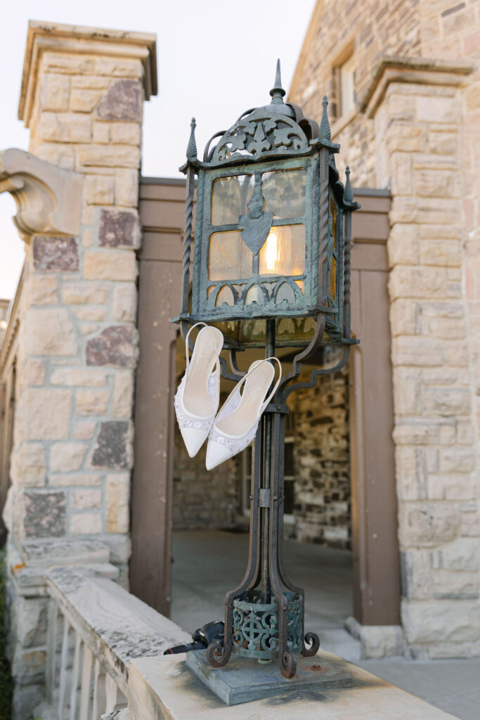 White bridal heels hanging in an editorial style from a vintage lantern at Highlands Ranch Mansion.