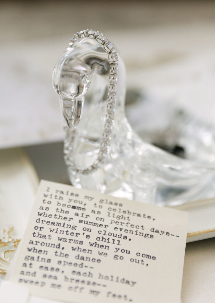 Diamond tennis bracelet draping off a romantic glass swan in a wedding details flat lay styled with a personal poem. 