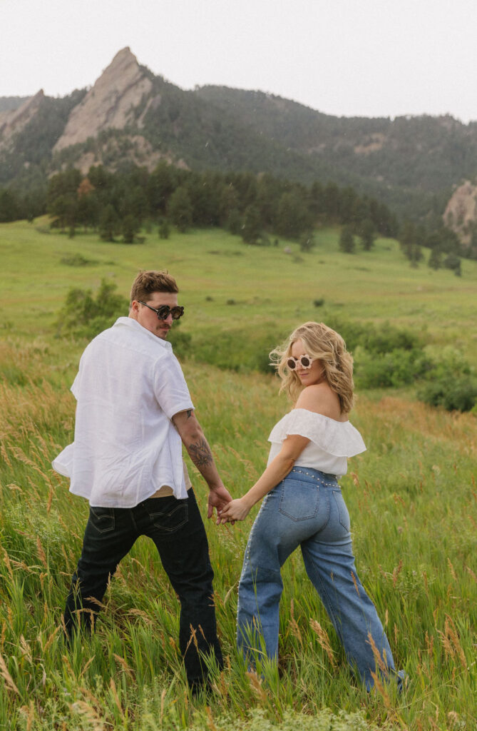 Playful moment of Paige and Austin wearing flower sunglasses surrounded by Colorado wildflowers at their Boulder engagement session