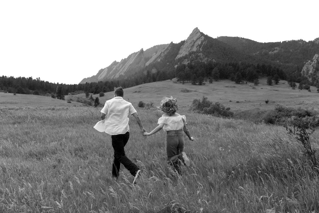 Couple running through wildflower field with raindrops sparkling in golden sunset light during Boulder engagement session