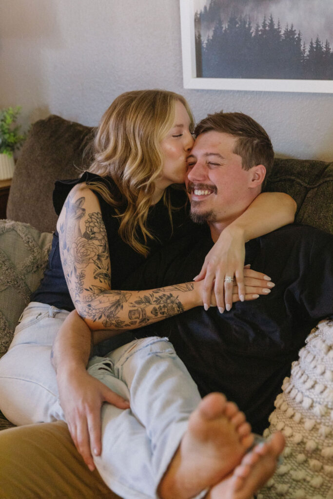 Couple cuddled up on their couch during a romantic in-home engagement session.