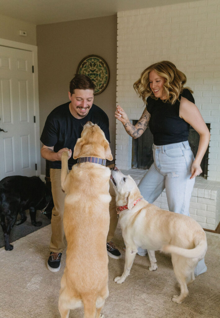 Candid moment of couple having a dance party with their dogs in their living room during their engagement photos.