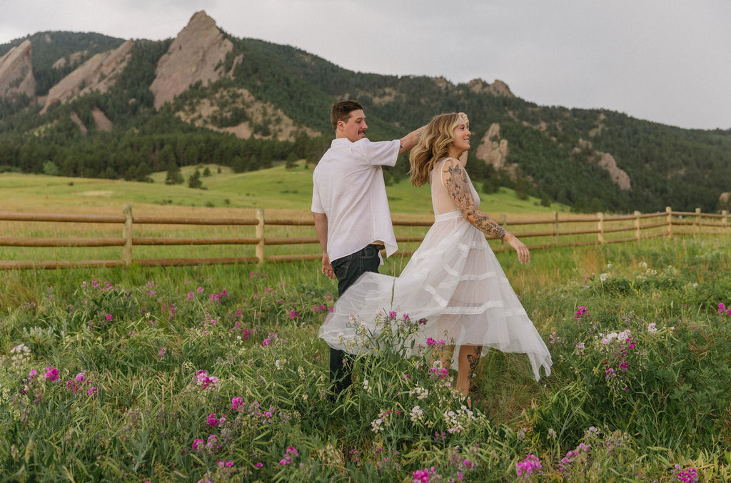 Boulder engagement photos featuring Flatirons backdrop and field of pink wildflowers at Chautauqua Park
