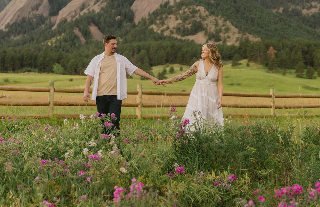 Couple holding hands among vibrant pink wildflowers at Chautauqua Park, best location for Colorado wildflower engagement photos