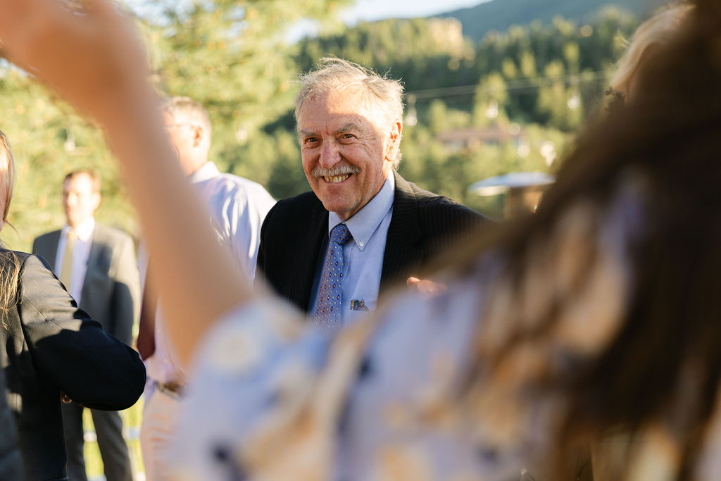 grandfather of groom smiling during outdoor Colorado wedding reception with mountain views and natural lighting