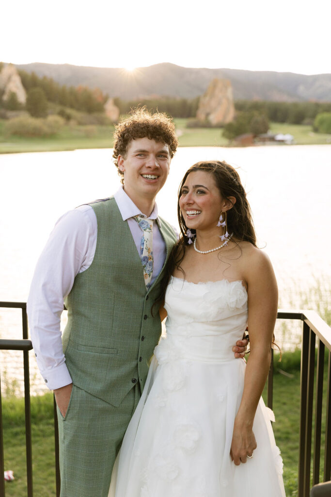 Newlyweds posing together in sage green vest and floral wedding dress at Colorado mountain wedding with sunset lighting