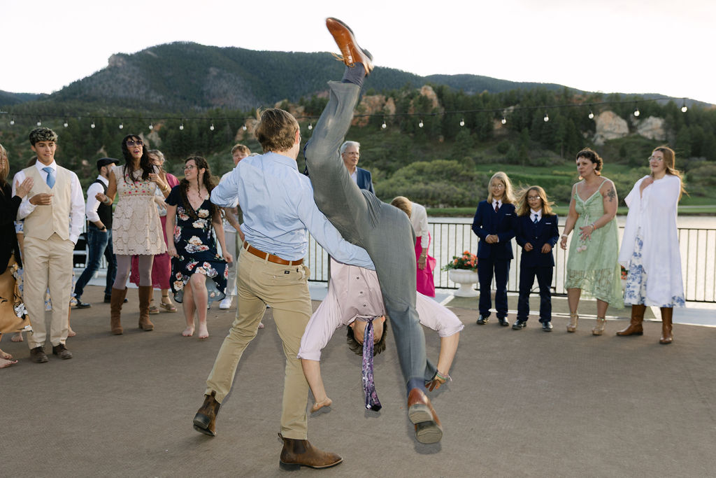 Wedding guests doing a backflip at the reception at outdoor Colorado venue with mountain backdrop