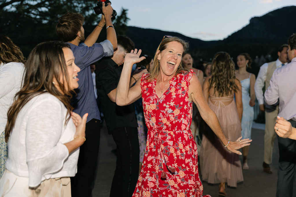 Wedding guest in red floral dress dancing and celebrating at outdoor Colorado mountain wedding reception