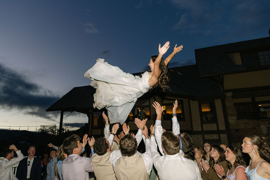 Bride being tossed in the air by wedding party at epic dancing reception outdoors