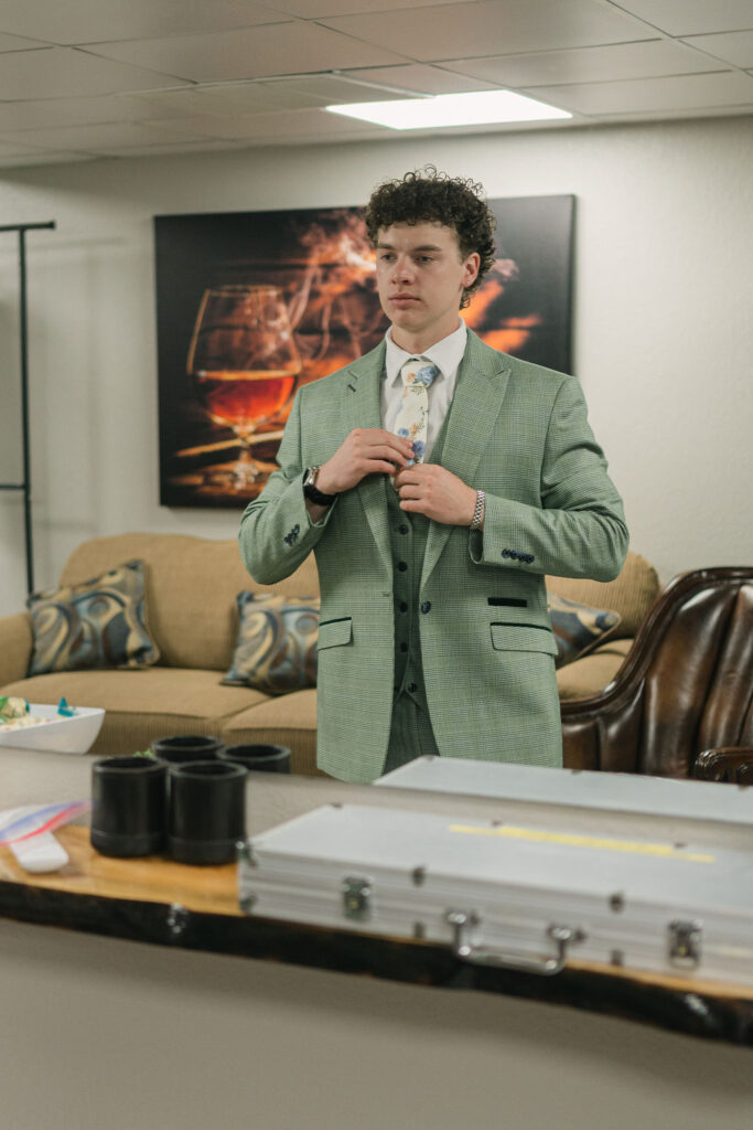 Groom getting ready in a light green suit in the groom suite at Perry Park