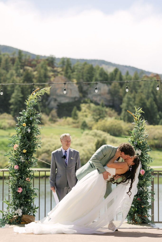 Gorgeous bride and groom first kiss during their mountain lakeside ceremony at Perry Park Country Club