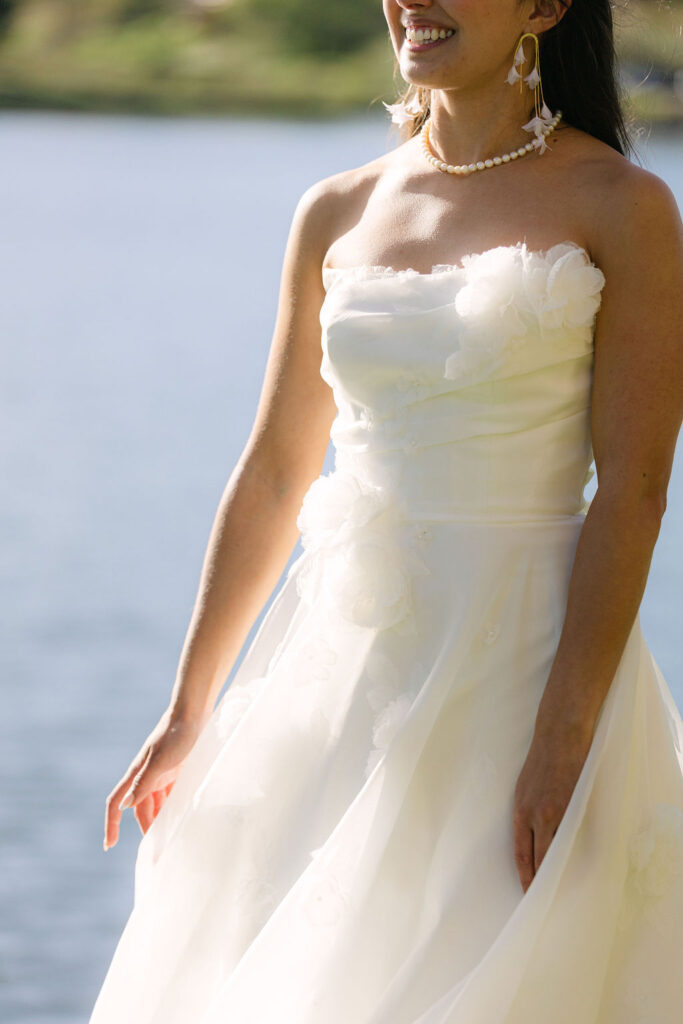 Bride in strapless wedding dress with pearl necklace by lake at elegant Colorado country club wedding