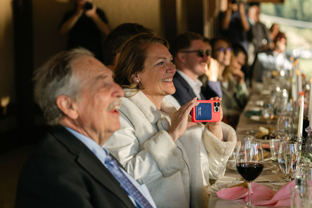Candid photo of wedding guest capturing toasts on phone during lakefront celebration at Colorado wedding venue
