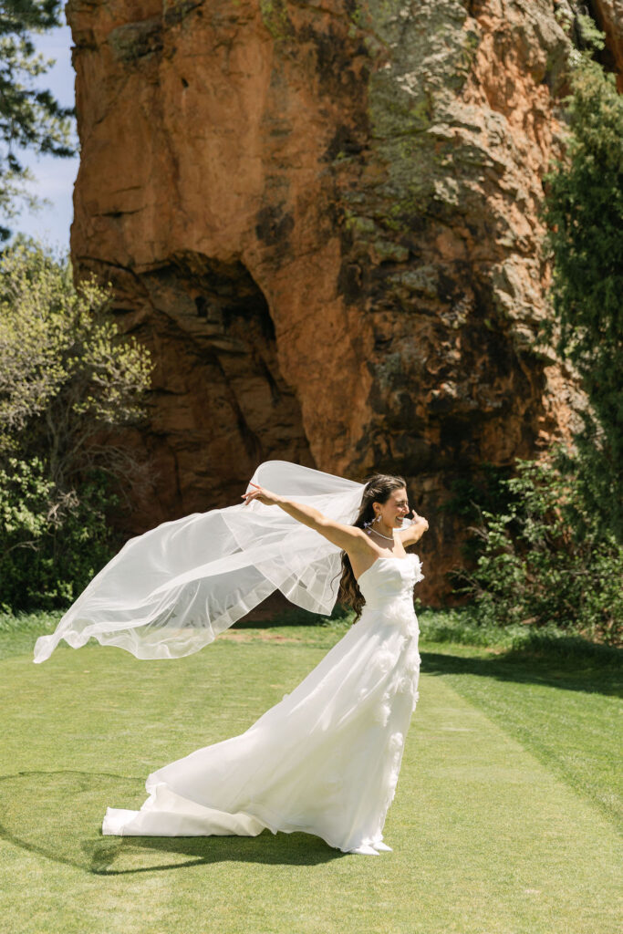 Bride in flowing wedding dress against red rock formations at Perry Park Country Club showing dramatic Colorado Front Range scenery