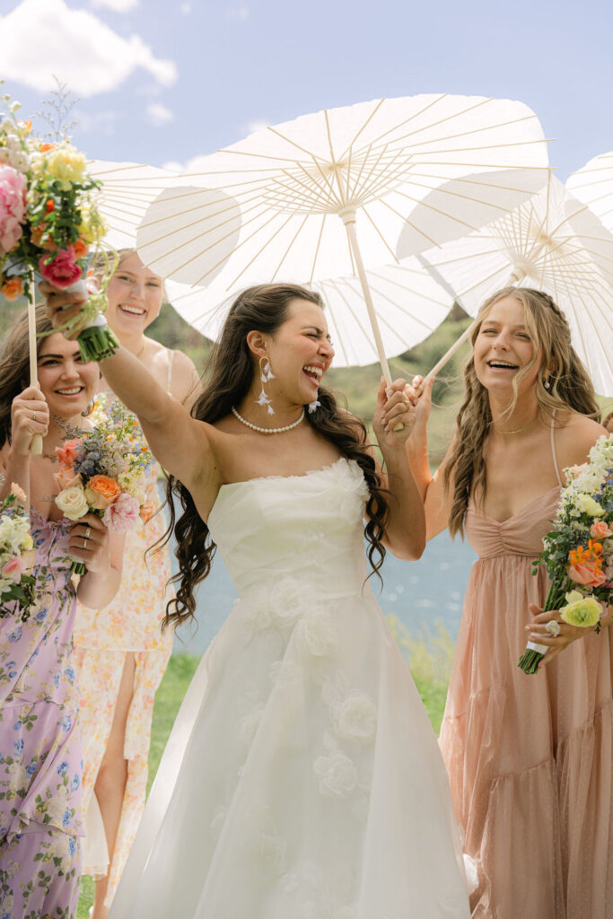 Bride joyfully cheering surrounded by her bridal party with parasols and colorful bouquets