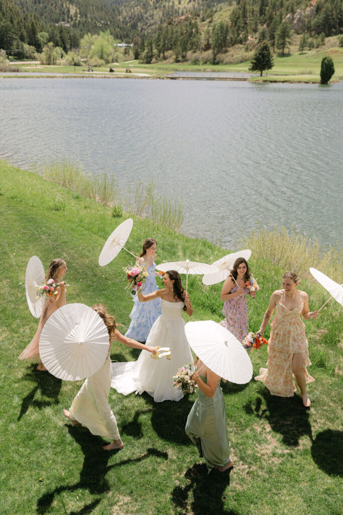 Bridal party with white parasols and colorful mismatched dresses by Lake Wauconda in Colorado