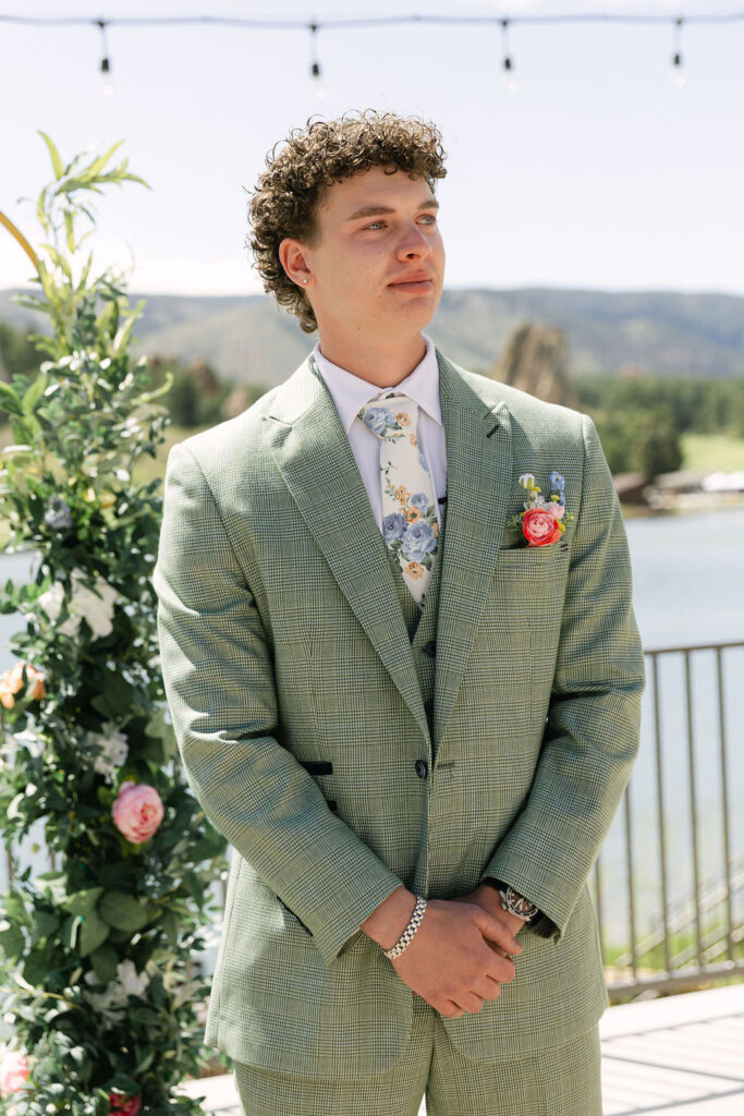 Groom in sage green checkered suit with floral tie at a lakeside Colorado wedding ceremony