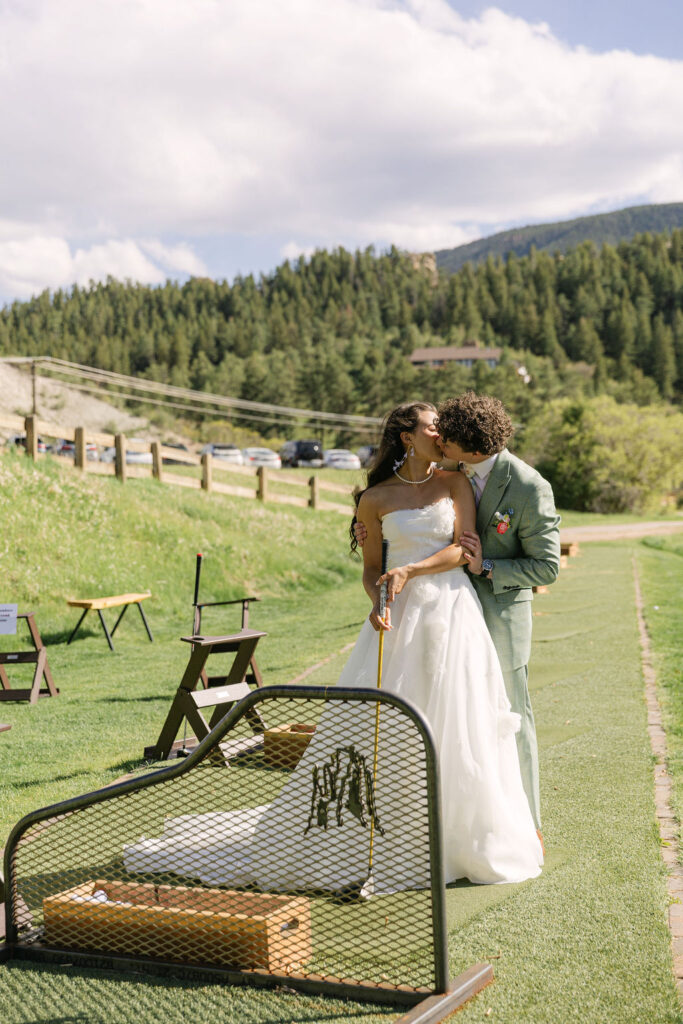 Bride and groom embracing at Perry Park Country Club driving range with Rocky Mountain foothills and pine trees in background during Colorado wedding