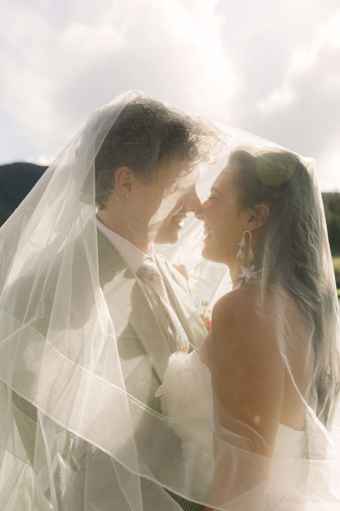 Intimate bride and groom portrait under flowing wedding veil at sunset