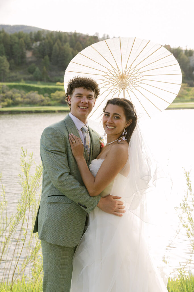 Bride and groom timeless portrait with a parasol by the lake at golden hour